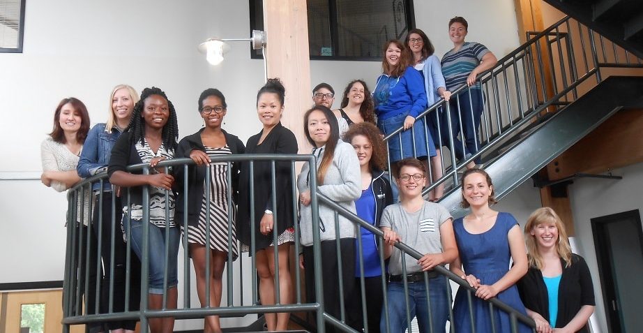 15 people of diverse backgrounds stand together along a multi-level staircase, smiling for a group photo.