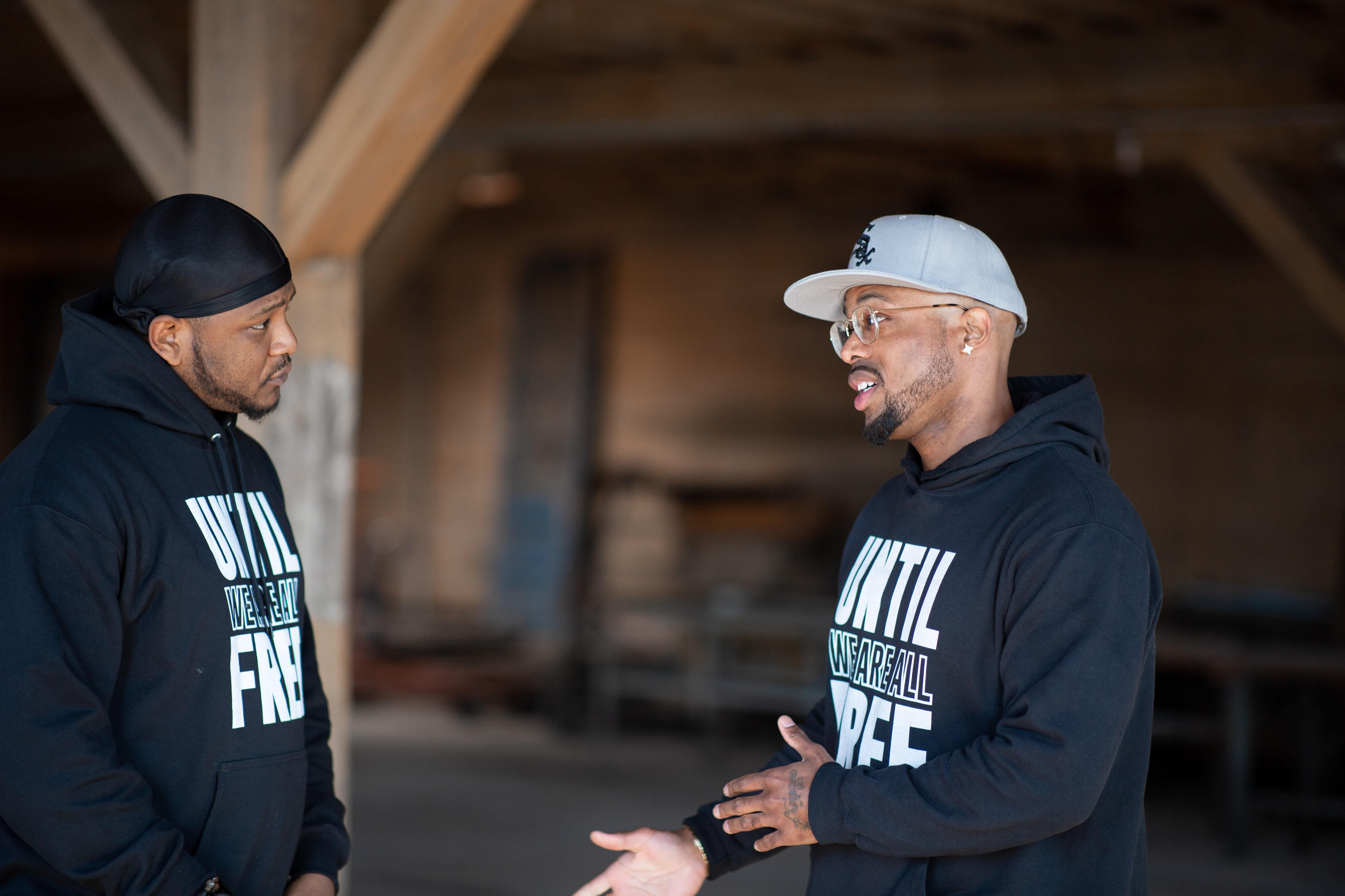 Two men talking to one another wearing hoodies that say "Until we are all free"